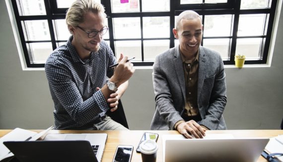 Two men smiling and using laptops