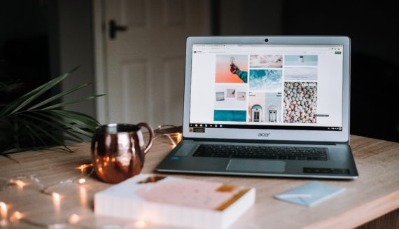 A laptop on a desk next to a book and a mug