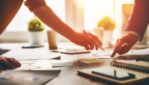 Two people pointing to sticky notes placed on a desk