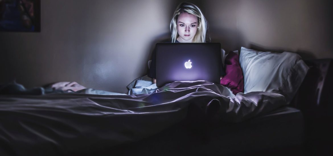 A woman sitting in the dark with a laptop on her lap