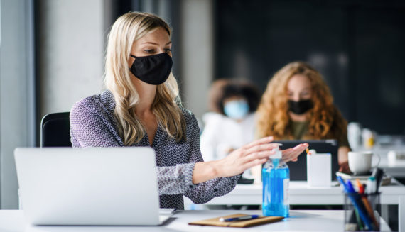 A woman wearing a mask and using hand sanitizer