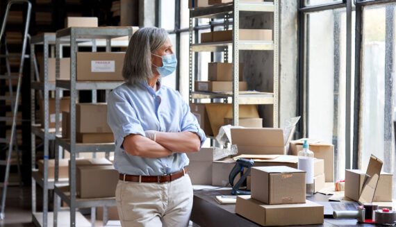 A person wearing a blue shirt and a mask standing in a storage